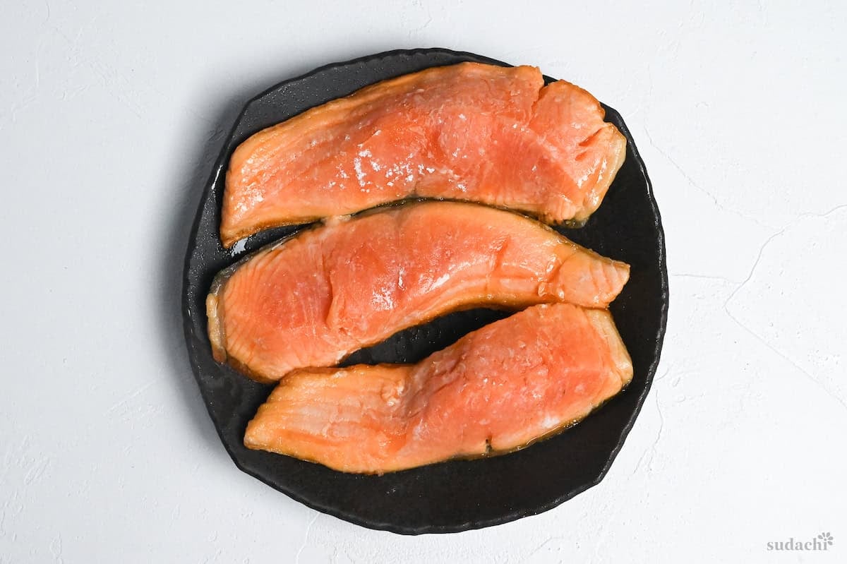 three partially cooked salmon fillets resting on a plate