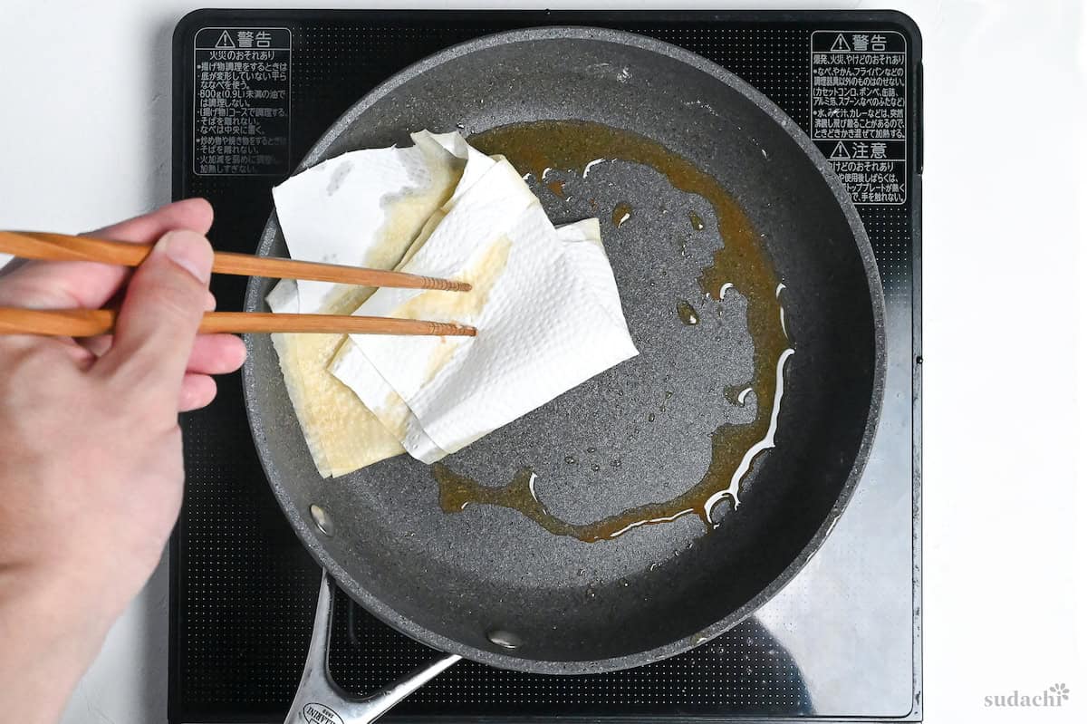 wiping excess oil out of a pan with kitchen paper held with chopsticks