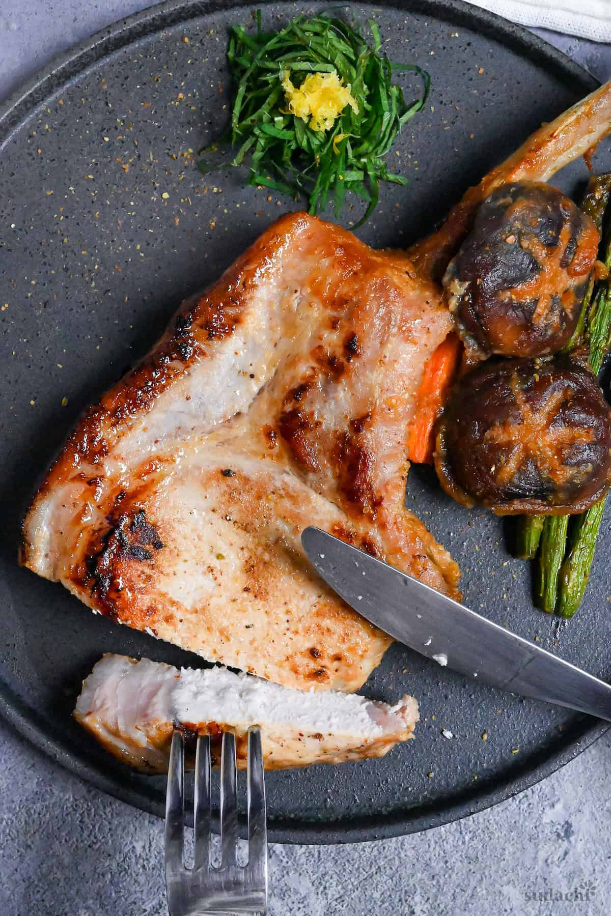 Miso marinated pork chop and roasted vegetables on a dark gray plate with shredded shiso leaves and yuzu peel