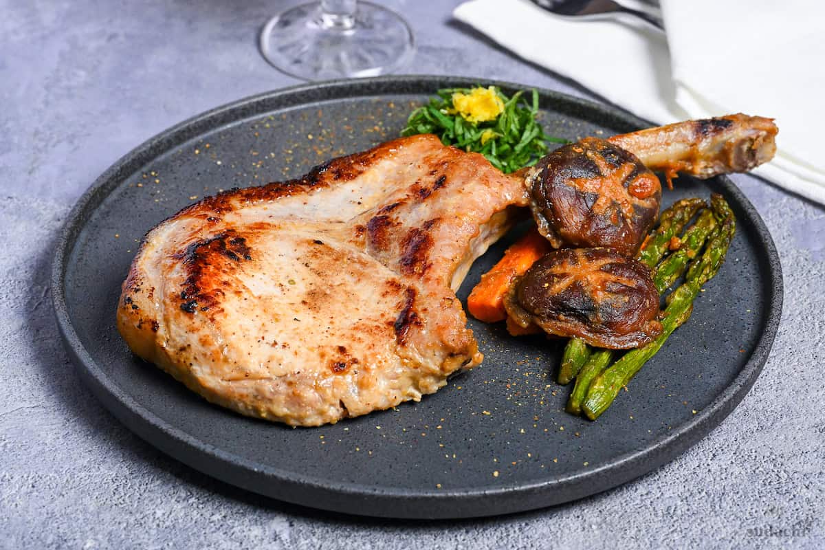 Miso marinated pork chop and roasted vegetables on a dark gray plate with shredded shiso leaves and yuzu peel
