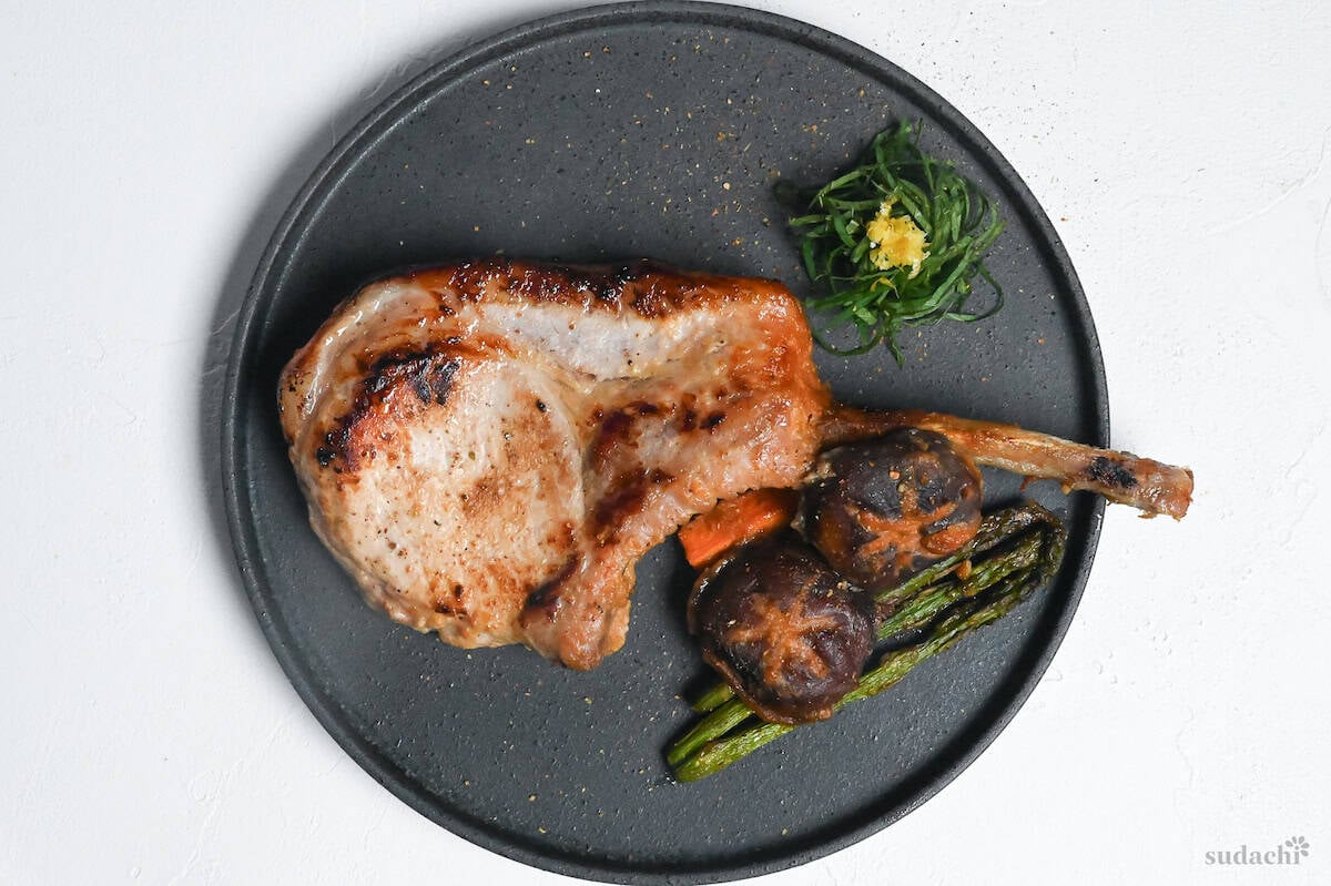 Miso marinated pork chop and roasted vegetables on a dark gray plate with shredded shiso leaves and yuzu peel