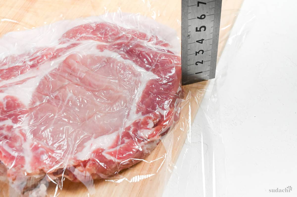 a bone-in pork chop on a bamboo cutting board with a metal ruler showing it's been pounded to 2cm thick