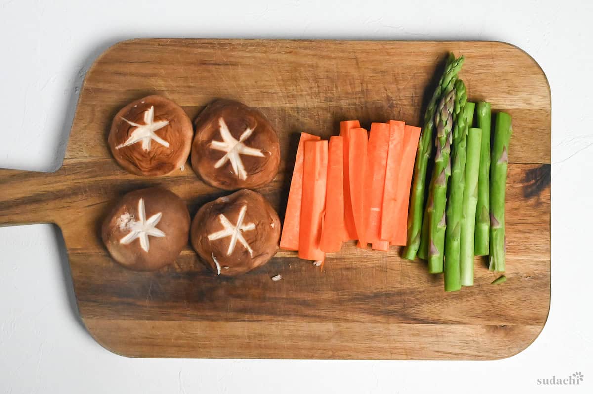 Shiitake mushrooms, carrots and asparagus on a wooden chopping board