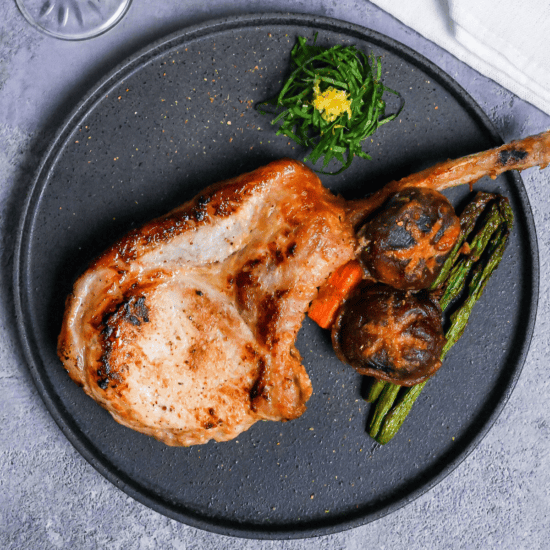 Miso marinated pork chop and roasted vegetables on a dark gray plate with shredded shiso leaves and yuzu peel
