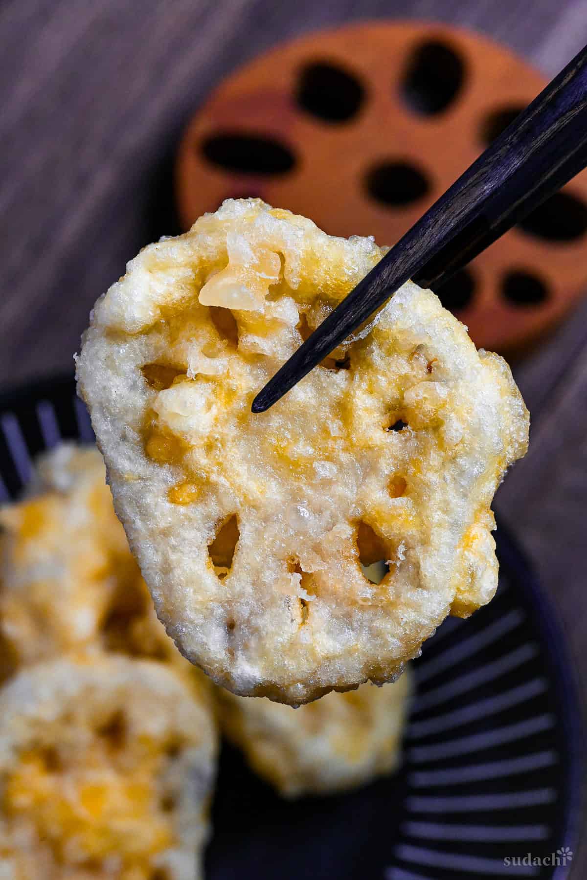 Once piece of renkon (lotus root) tempura held up with black chopsticks