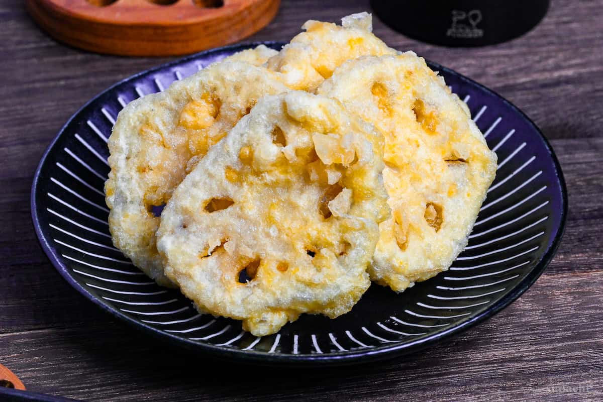 Five pieces of renkon tempura (lotus root) on a black plate with white stripes on a dark wooden background