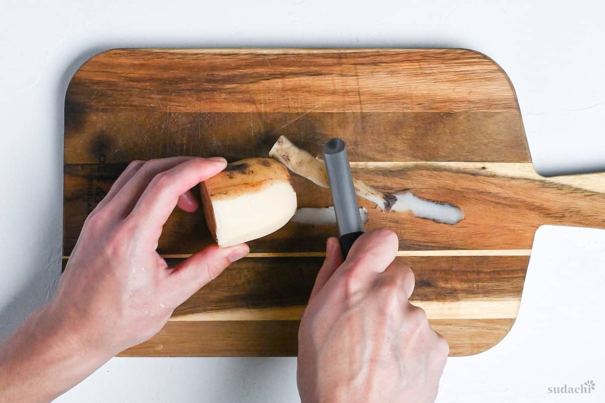 Peeling washed renkon (lotus root) on a wooden chopping board on white background