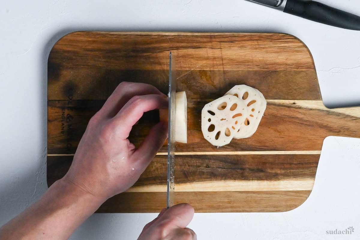 Cutting thick slices of renkon (lotus root) on a wooden chopping board on white background