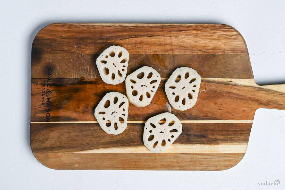 Thick slices of lotus root (renkon) on a wooden chopping board on white background