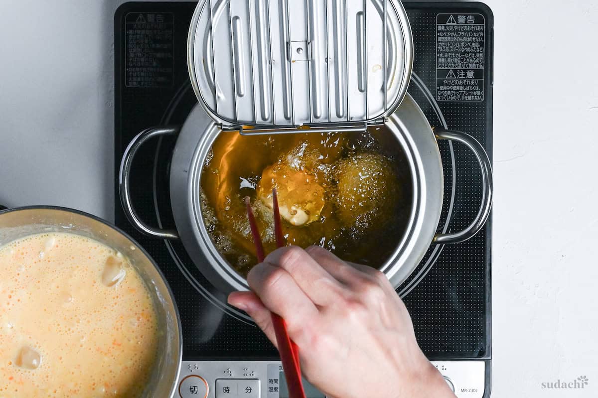 Tempura battered renkon (lotus root) being placed in pot of oil