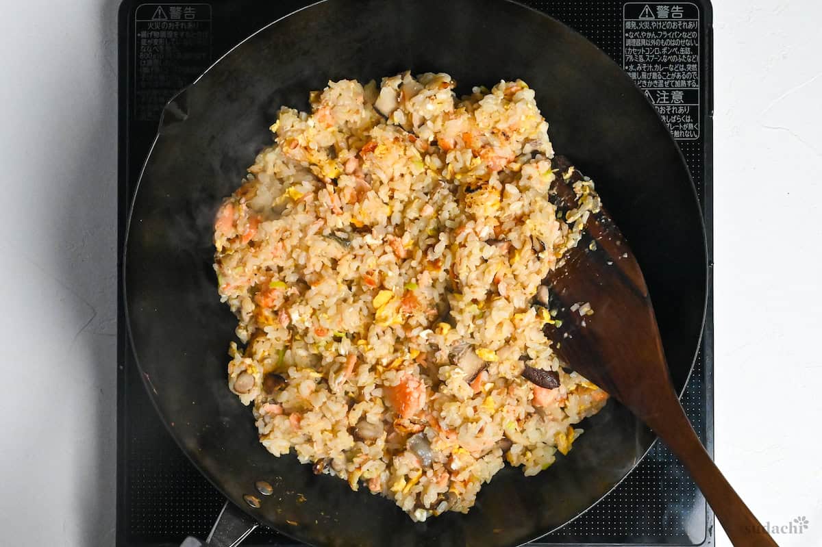 salmon fried rice in a wok with wooden spatula on the stovetop