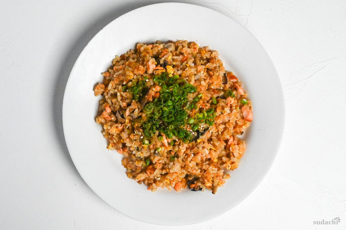 salmon fried rice on a white plate garnished with chopped green onions and toasted white sesame seeds
