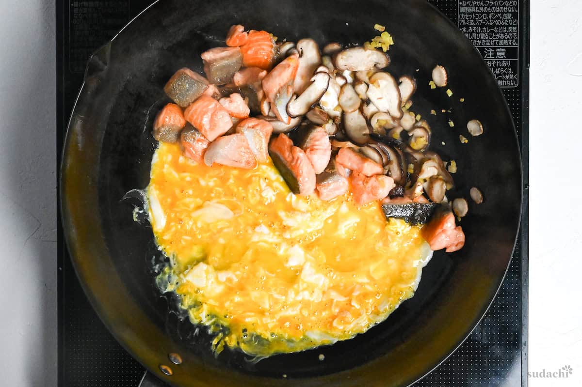 cooked salmon, mushrooms and ginger next to egg in a wok on the stove