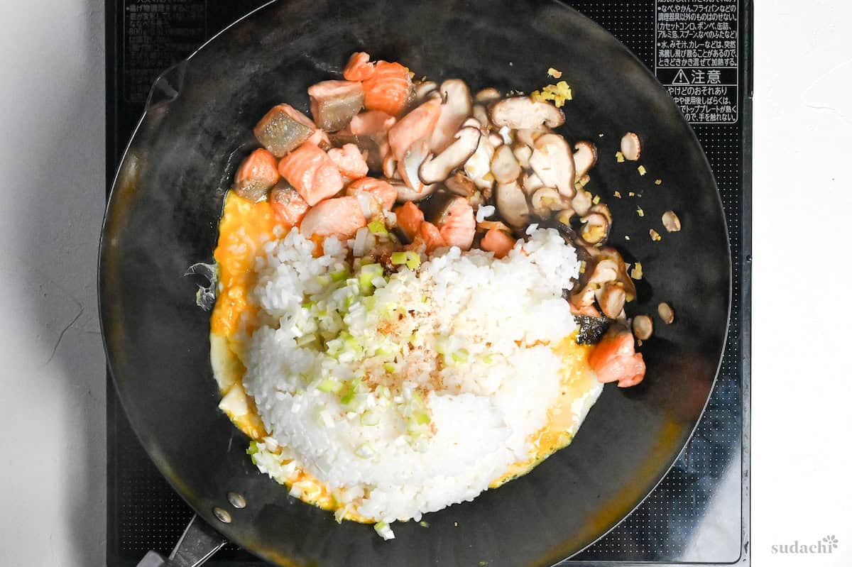 rice and finely chopped Japanese leek in a wok with salmon, mushrooms and ginger