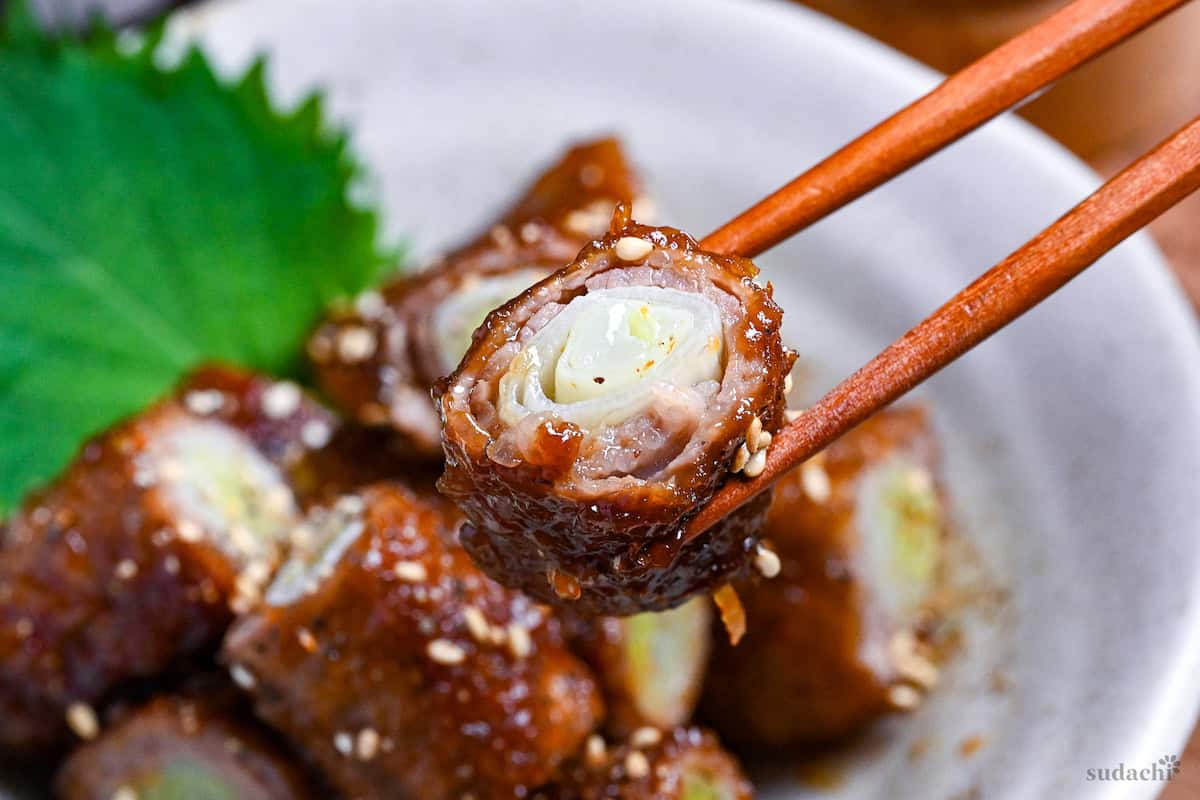 holding up one bitesize piece of beef negimaki up with wooden chopsticks