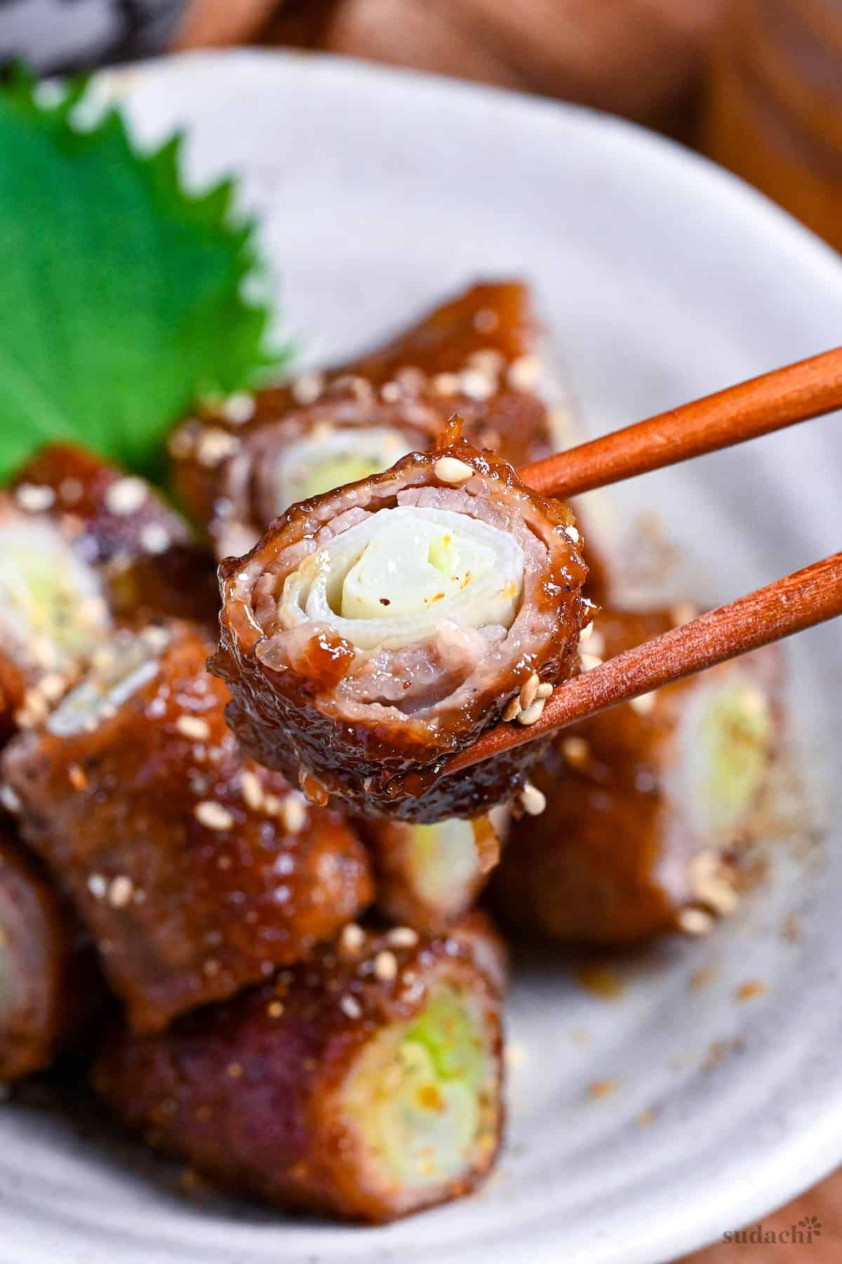holding up one bitesize piece of beef negimaki up with wooden chopsticks