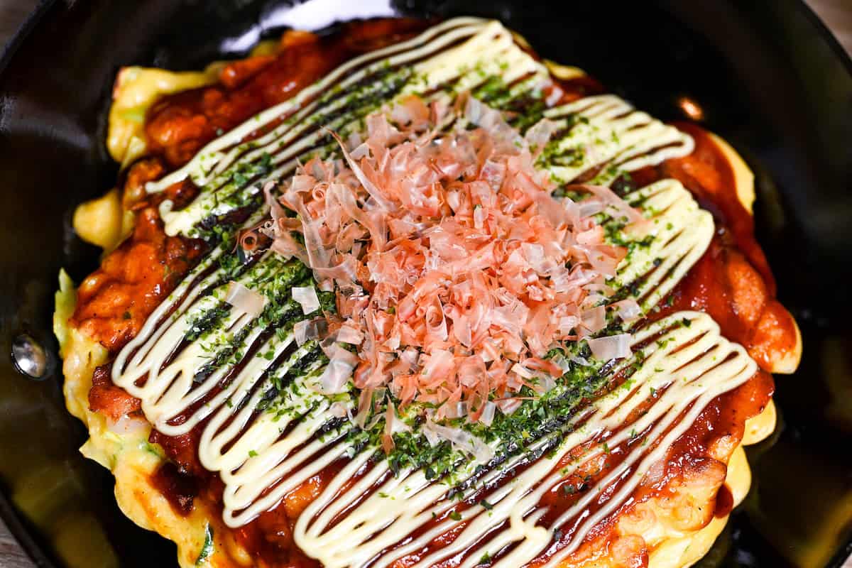 Osaka style okonomiyaki topped with homemade okonomi sauce, mayonnaise, aonori and bonito flakes in a small frying pan