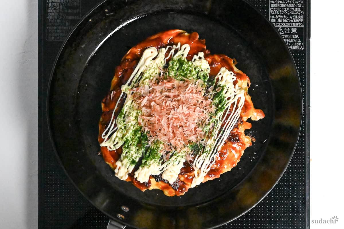 okonomiyaki topped with okonomi sauce, mayonnaise, aonori and bonito flakes in a cast iron frying pan