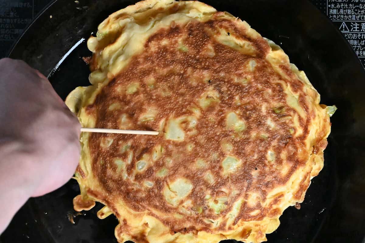 Piercing okonomiyaki with a bamboo skewer to check doneness