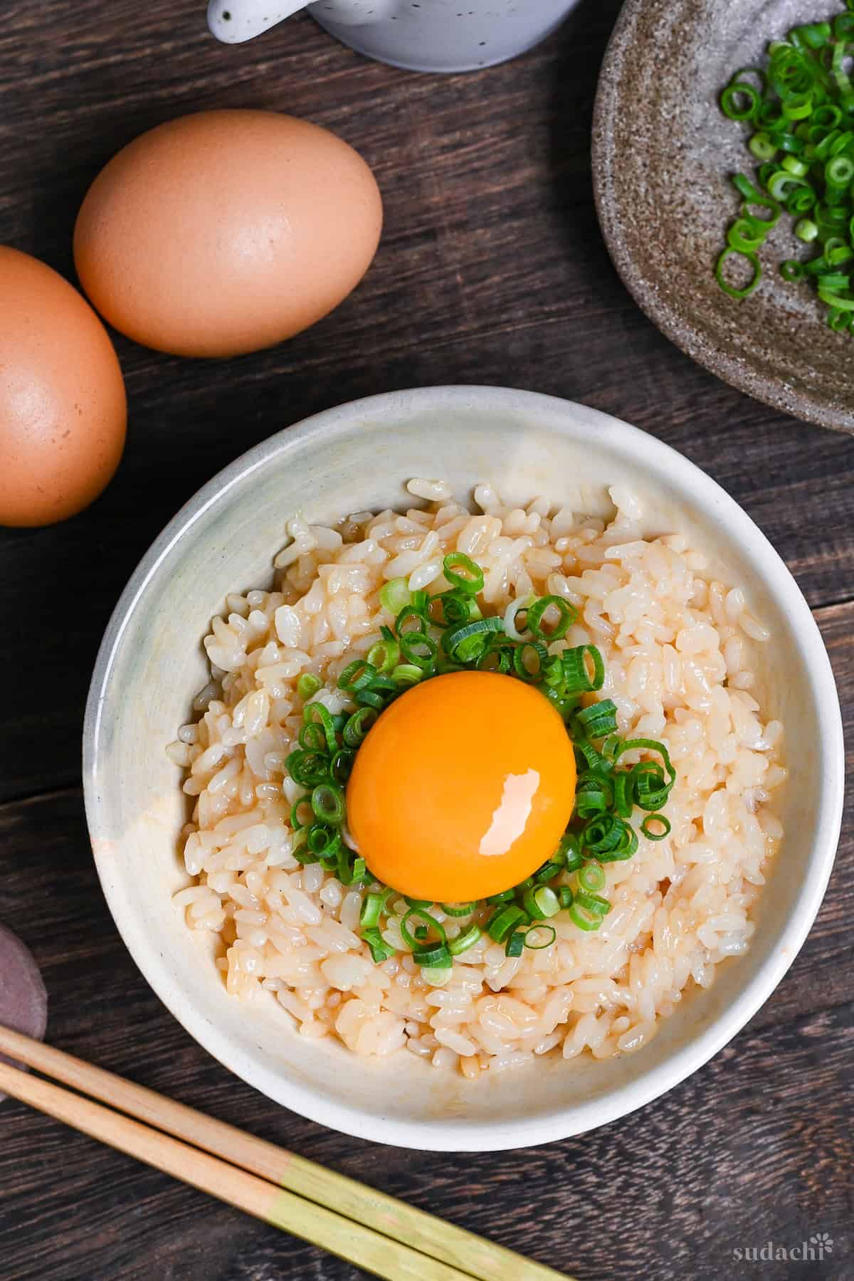 Tamago kake gohan topped with chopped green onions and a raw egg yolk in a cream ceramic bowl top down