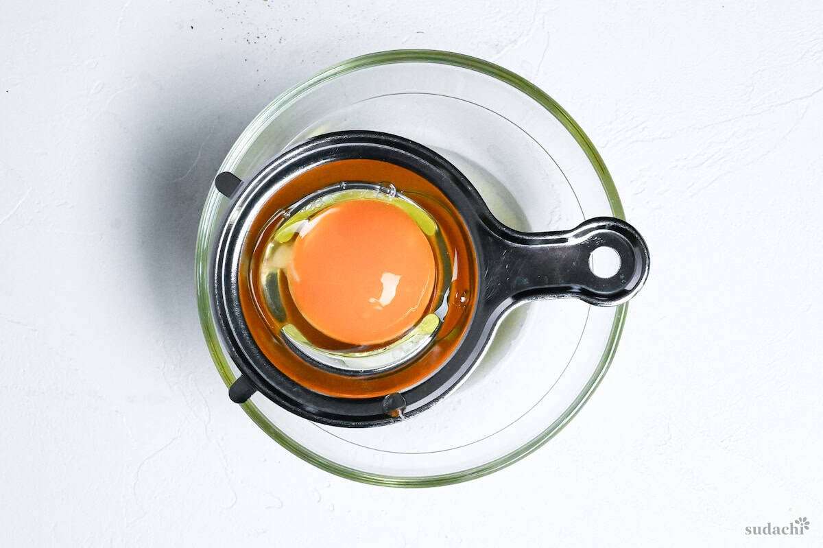 An metal egg separator over a glass bowl with an egg yolk inside