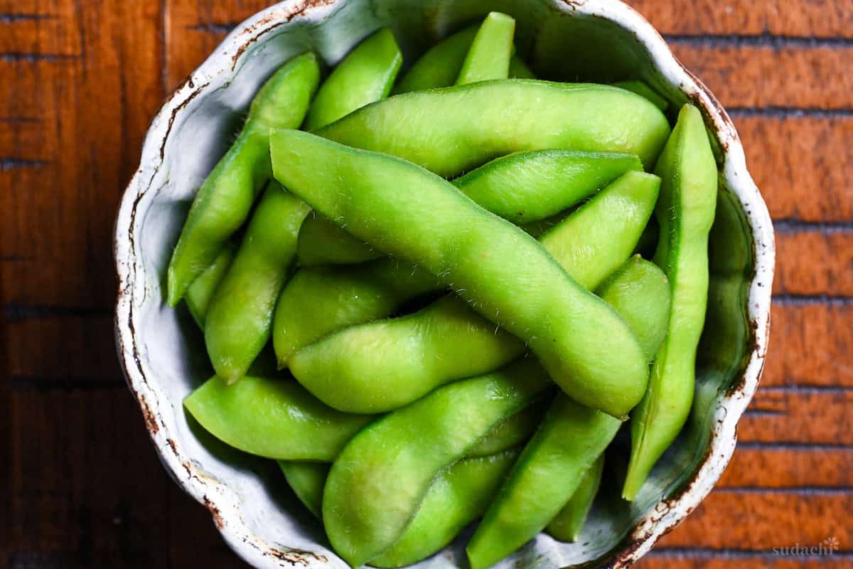 Izakaya style salt boiled edamame in an off-blue bowl on a wooden table with black lines