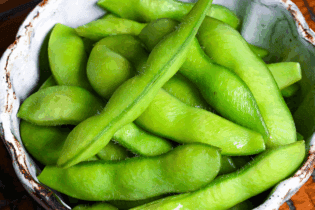 Izakaya style salt boiled edamame in an off-blue bowl on a wooden table with black lines