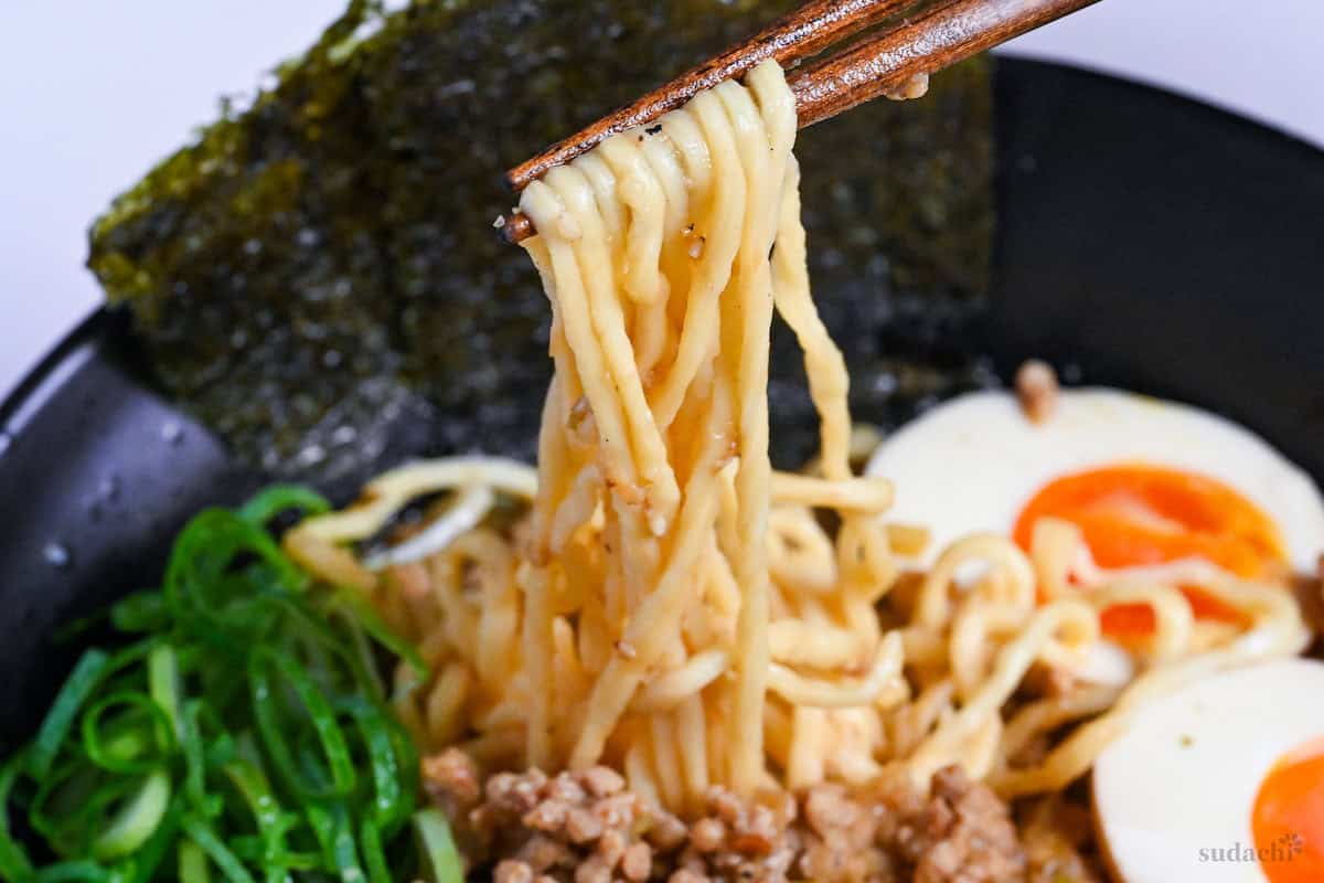 wooden chopsticks pulling up homemade egg ramen noodles in a bowl of miso ramen