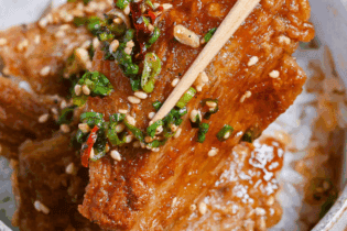 Close up of sauce coated crispy enoki mushrooms held up with wooden chopsticks