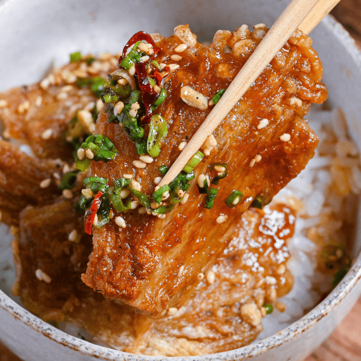 Close up of sauce coated crispy enoki mushrooms held up with wooden chopsticks