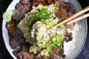 picking up gyutan covered with negi shio sauce with wooden chopsticks