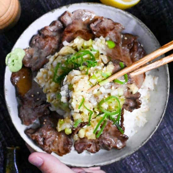 picking up gyutan covered with negi shio sauce with wooden chopsticks