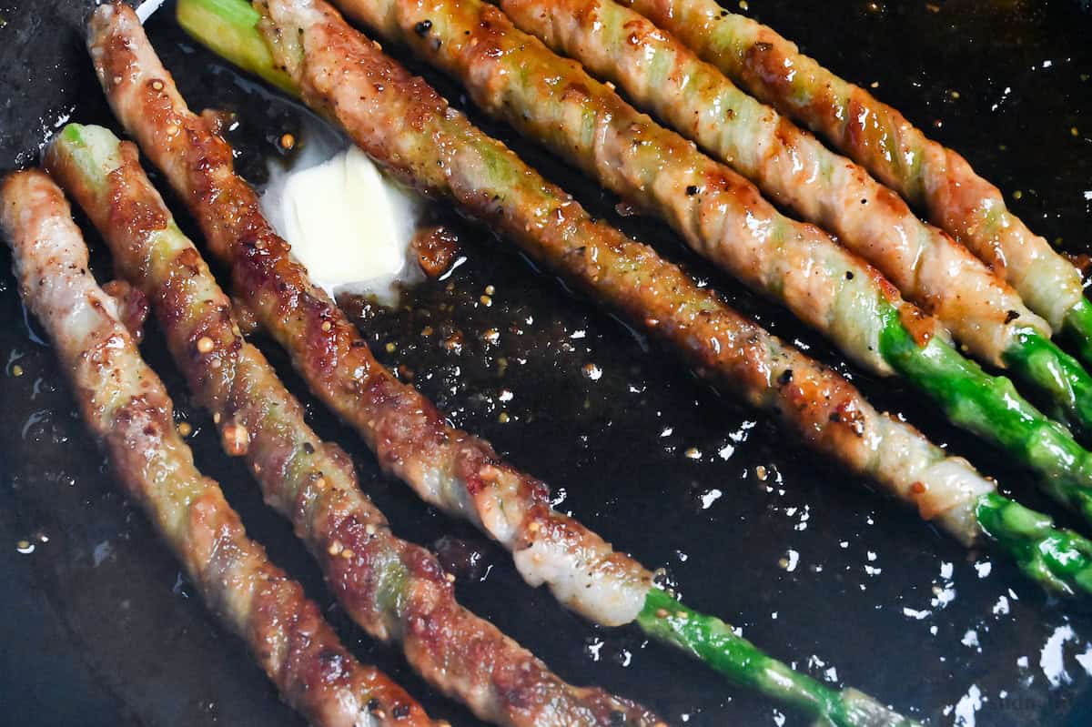 Nikumaki (pork belly wrapped) asparagus frying in a pan with butter and sauce