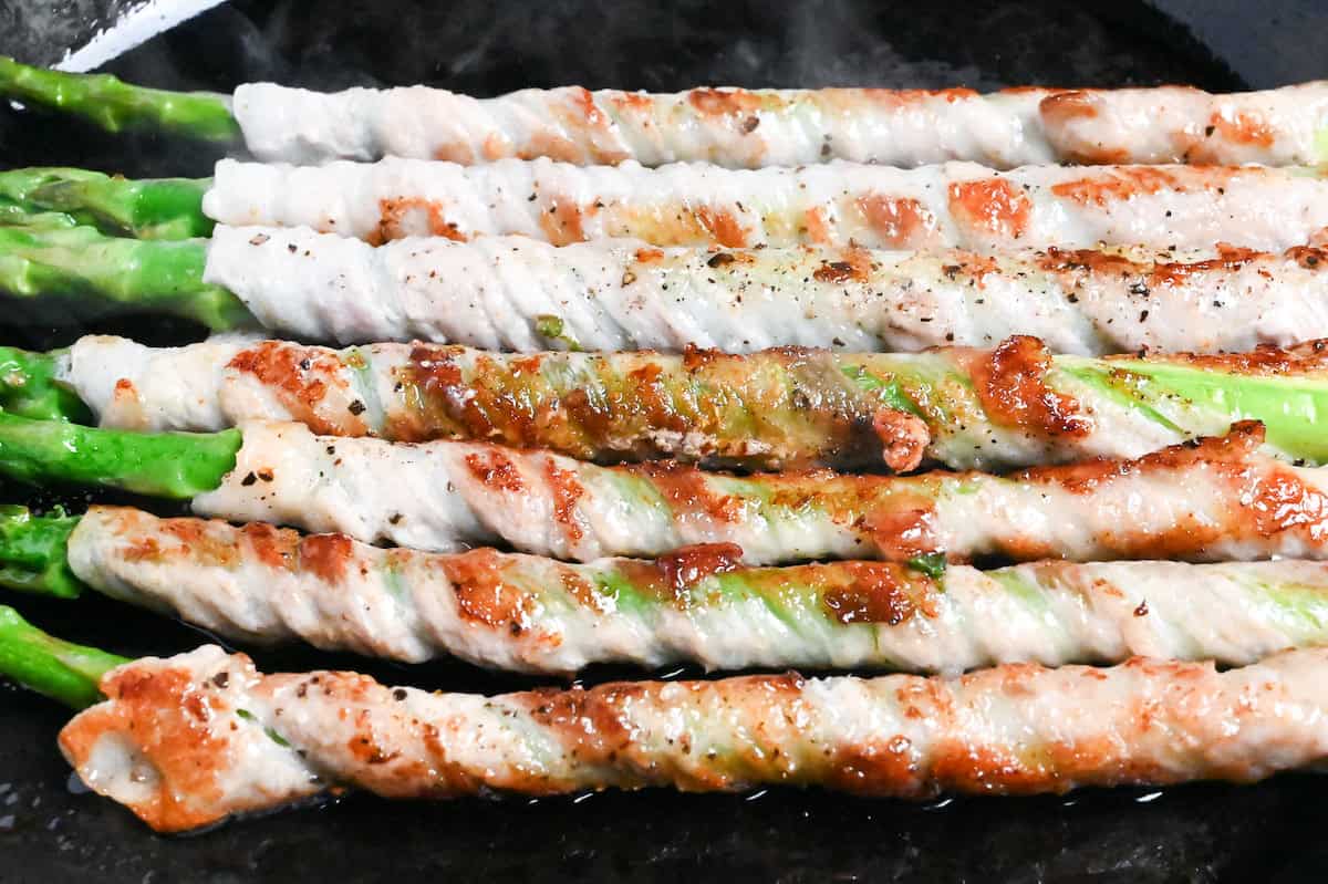 Close up of nikumaki (pork belly wrapped) asparagus in a frying pan