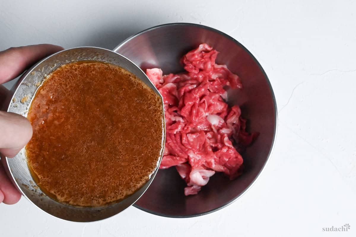 pouring pepper rice sauce over beef in a steel mixing bowl on a white background