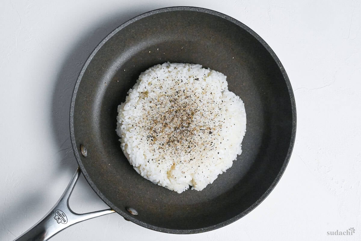 cooked rice in the center of a frying pan topped with ground black pepper