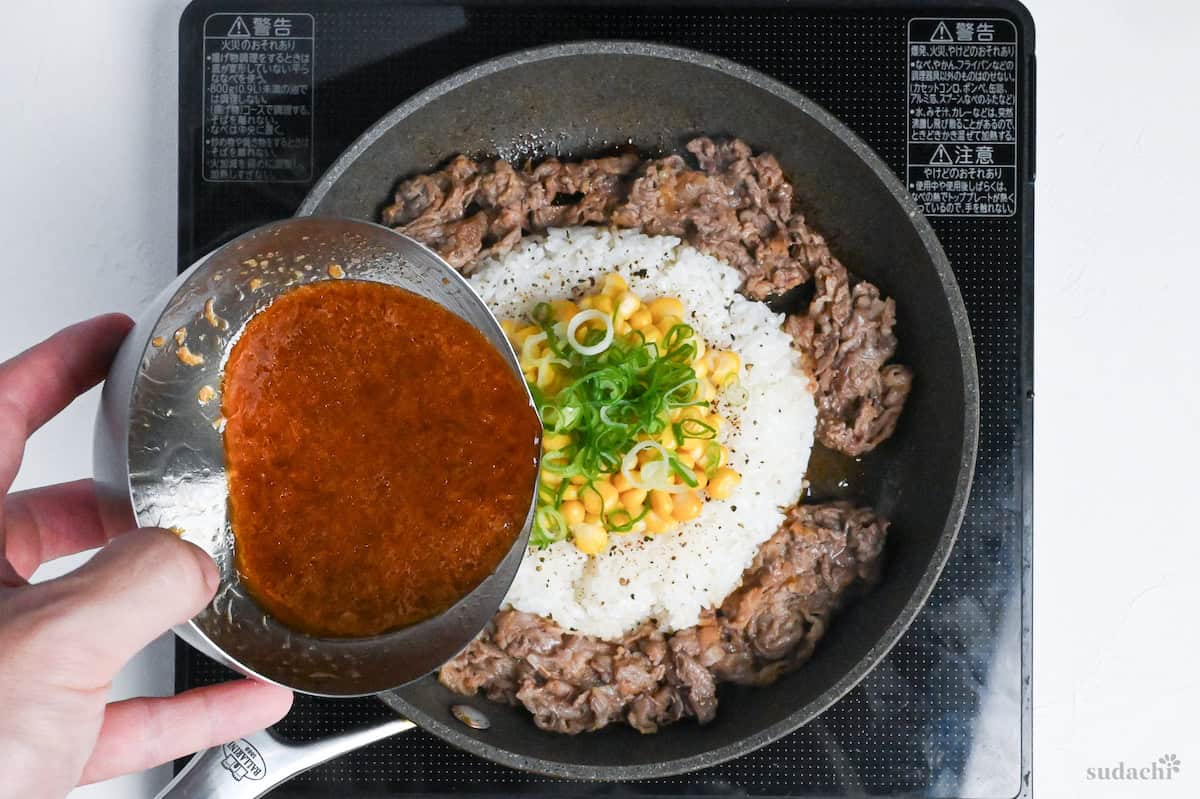 pouring sauce over beef pepper rice in a frying pan on the stove