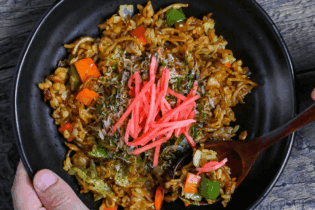 scooping a spoonful of soba-meshi from a black plate next to salt and pepper grinders