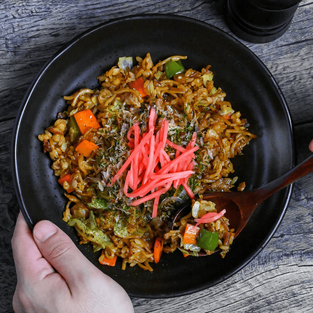 scooping a spoonful of soba-meshi from a black plate next to salt and pepper grinders