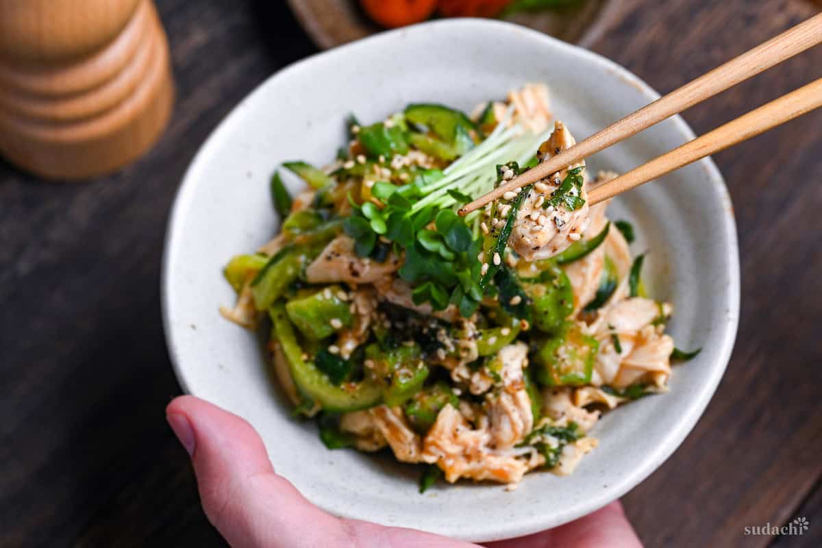 Poached Chicken Tender Salad with Fruity Japanese Style Dressing in a white dish held in a hand, with chopsticks holding up a piece of chicken