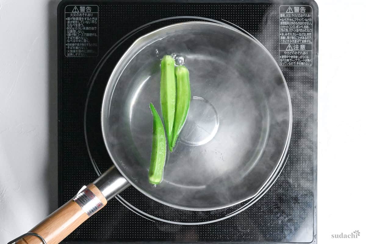 3 okra boiling in a pot of water on the stove top