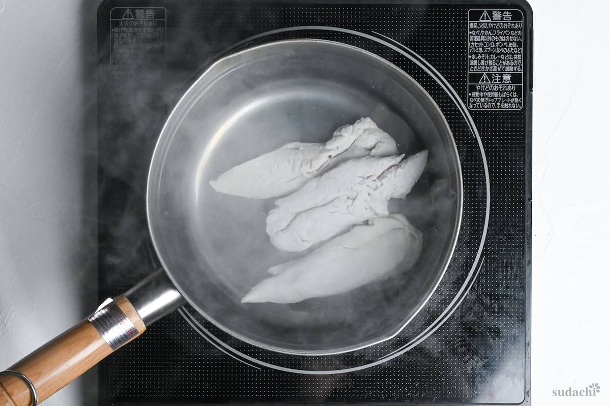 3 chicken tenders in boiling water in a pot on the stove top