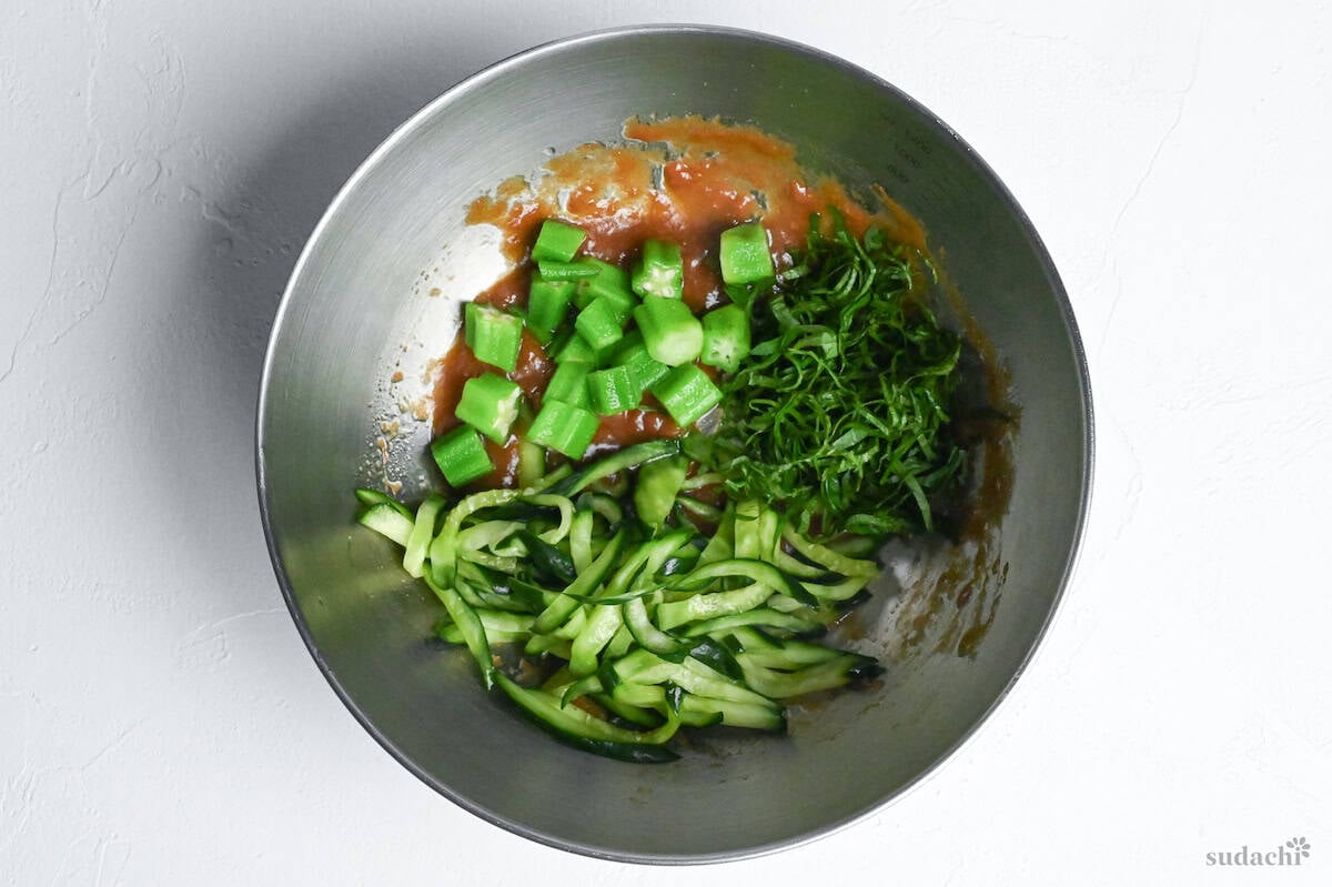 julienned cucumber, shredded shiso and thick cuts of okra in dressing in a bowl for chicken tender salad