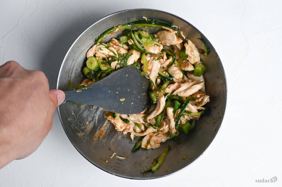 poached and shredded chicken tenderloins with vegetables and Japanese style dressing in a bowl on a white background