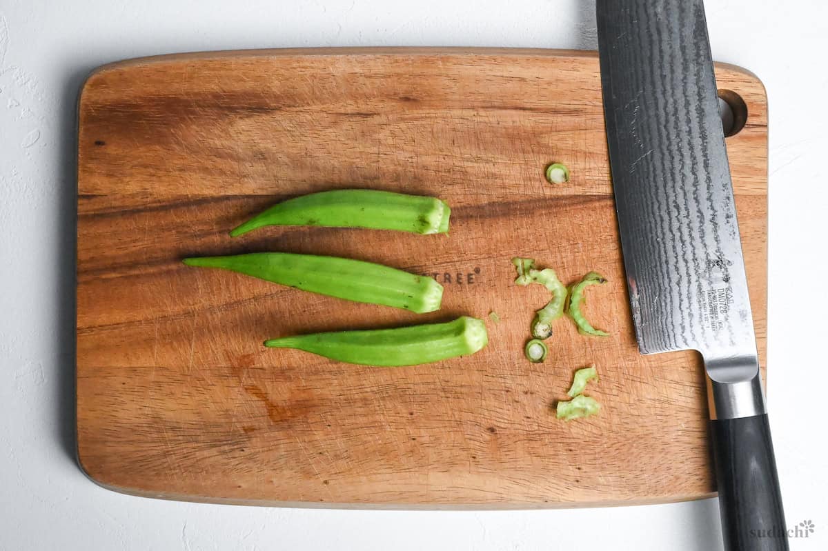 three okra with peeled tops on a wooden cutting board on a white background