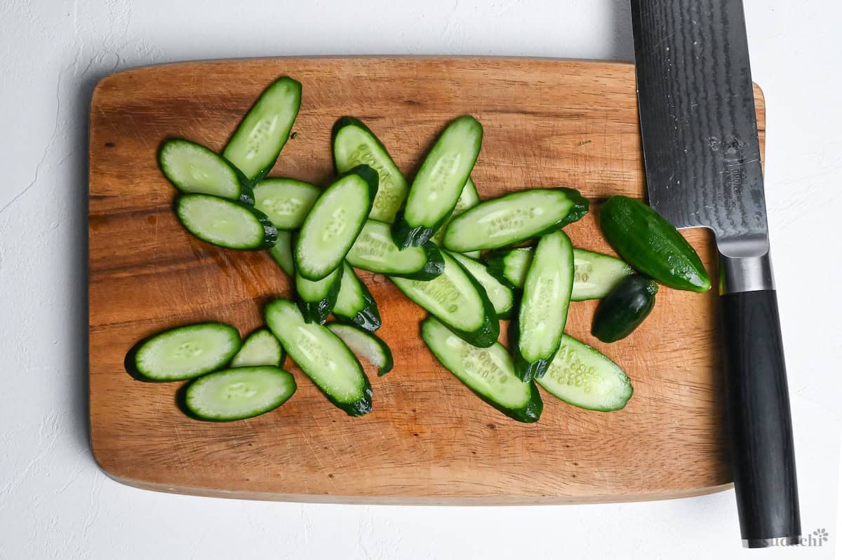 sliced cucumber on a wooden cutting board with vegetable knife