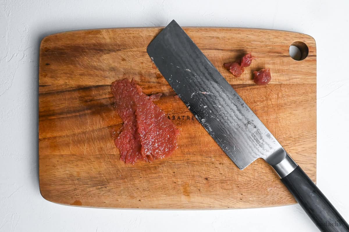 pasted umeboshi on a wooden cutting board with vegetable knife