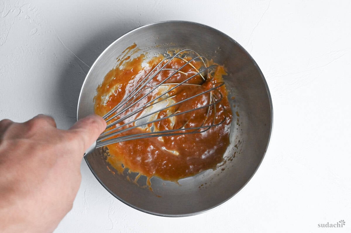 Japanese inspired chicken tender salad dressing being whisked in a steel mixing bowl on a white background