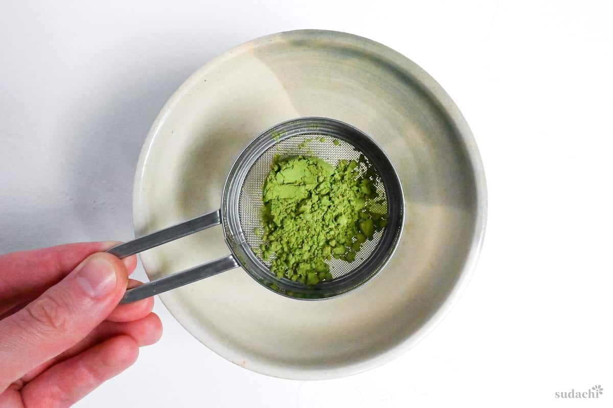 sifting matcha into a ceramic bowl