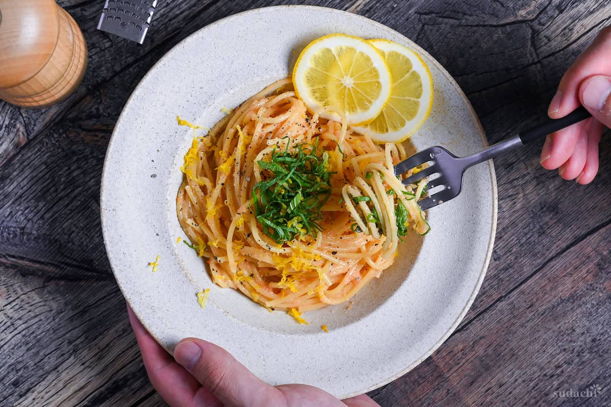 Top down of hand holding fork and lifting mentaiko pasta from plate